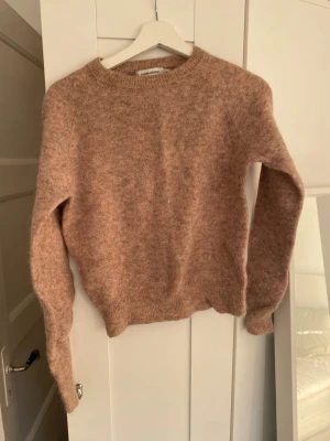 Beige fluffig stickad tröja - Mysig beige stickad tröja från Carin Wester i fluffigt material. Tröjan har rund halsringning, långa ärmar och ribbade muddar vid ärmslut och nederkant. Perfekt för kalla dagar och enkel att matcha med jeans eller kjol. 