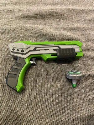 Grön och grå Beyblade launcher - Säljer en Beyblade launcher i plast med cool design i grönt, grått och svart. Medföljer en matchande Beyblade-topp som passar perfekt till launchern. Perfekt för dig som gillar att utmana kompisarna i Beyblade-strider!