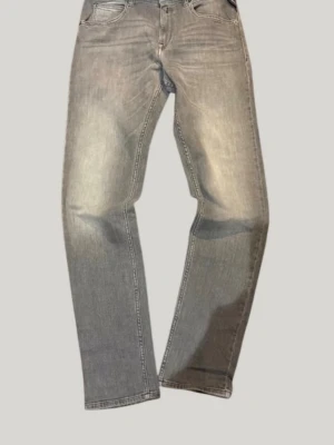 Grå replay jeans med vintagekänsla - Säljer ett par grå jeans med rak passform och klassisk femficksdesign. Jeansen har en snygg tvättad look och subtila slitningar för en vintage vibe. Perfekta till sneakers eller boots och passar till många olika stilar.