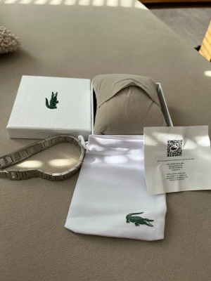 Silver armband från Lacoste - Säljer ett stilrent armband i rostfritt stål. Silverfärgad design med moderna länkar som passar både till vardag och fest.  ✔ Rostfritt stål – tåligt och håller färgen ✔ Minimalistisk och trendig look ✔ Unisex – passar alla ✔ Sparsamt använt / i mycket bra skick ✔ Kommer med originalförpackning  Perfekt som present eller för att uppgradera din egen stil ✨