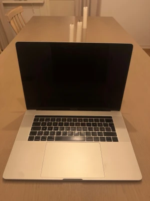 MacBook Pro 15 tum silver - Snygg och stilren MacBook Pro 15 tum i silver med stor touchpad och bakbelyst tangentbord. Tunn och lätt design i aluminium, perfekt för både plugg och kreativt arbete. Klassisk Apple-logga på locket och svart ram runt skärmen.