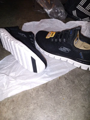Nya Svarta Skechers Glide-Step sneakers stl 42/43 - Svarta Skechers Glide-Step sneakers med vit, chunky sula och mesh-överdel. Skorna har elastiska snören, diskret logga på sidan och detaljer i blått. Lätta och flexibla med sportig look, perfekta för dig som gillar streetstyle. Stl 42 men passar även 43..Nya.