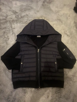 Moncler cardigan  - Navy blue moncler cardigan med stickade ärmar och stor huva. Jackan har två framfickor med tryckknappar och en dragkedja på vänster ärm. Perfekt för kalla dagar Priset går att diskutera 