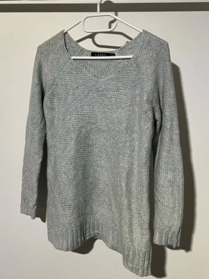 Ljusgrå stickad tröja Lauren Ralph Lauren - Ljusgrå stickad tröja från Lauren Ralph Lauren med v-ringning och långa ärmar. Tröjan har ribbstickade muddar vid ärmslut och nederkant samt en något längre passform. Perfekt för lager på lager och enkel att matcha.