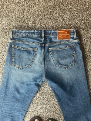 Blå jeans från Jacob Cohen - Säljer ett par blå jeans från Jacob Cohen med klassisk femficksdesign och rak passform. Jeansen har snygga kontrastsömmar, läderpatch med logga bak och är gjorda i mjukt denimtyg. Perfekta för en avslappnad men ändå stilren look storleken är 33 men sitter mindre som typ 31/32