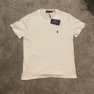 Vit t-shirt från Polo Ralph Lauren - STÅR L MEN PASSAR S!!!     Klassisk vit t-shirt från Polo Ralph Lauren med liten broderad logga på bröstet. T-shirten har rund hals, korta ärmar och är tillverkad i mjuk bomull för en skön känsla. Perfekt basplagg till garderoben.