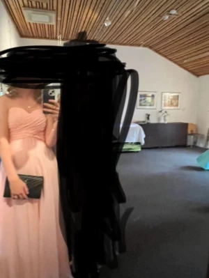 Ljusrosa axelbandslös långklänning - Säljer en elegant ljusrosa långklänning med axelbandslös design och vackert draperad överdel. Klänningen har en utsvängd kjol och är perfekt för bal eller student. Materialet känns lätt och flytande, troligen polyester eller liknande.