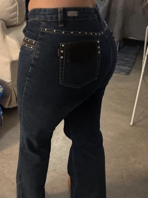 Mörkblå jeans med nitar  - Säljer ett par mörkblå bootcut jeans med nitar. Jeansen har detaljer på bakfickorna. Midja ca 80 cm. Innerbenslängd ca 82 cm. Benlängd ca 110 cm. Nypris 800 kr💕 Storlek M