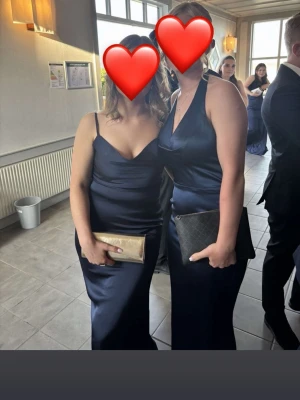 Marinblå långklänning i satin - Elegant marinblå långklänning i satin med smala axelband och v-ringad halsringning, använd 1 gång. Klänningen har en figurnära passform och är köpt på Bubbleroom för 1299kr, dock säljs inte mer.