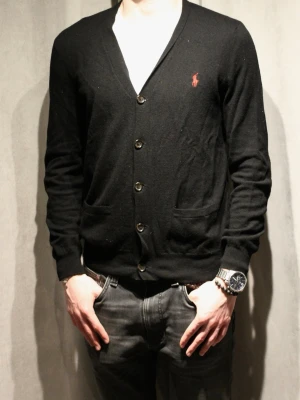 Svart merinoull kofta från Polo Ralph Lauren - Svart kofta med knäppning framtill från Polo Ralph Lauren. Klassisk design med två fickor, brunt logobroderi på bröstet och bruna mockadetaljer på armbågarna. Perfekt för lager-på-lager och snygg till jeans. Modellen är 182 cm lång🌟 hör av dig vid frågor ✌🏻