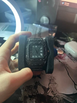 Klocka - Snygg svart klocka med fyrkantig urtavla och romerska siffror. Klockan har ett detaljerat armband och boett dekorerad med svarta stenar för en lyxig känsla. Passar perfekt för dig som gillar statement-accessoarer.