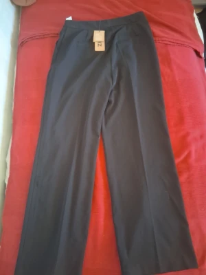 Svarta kostymbyxor från Zign - Snygga svarta kostymbyxor från Zign med raka, vida ben och hög midja. Byxorna har en minimalistisk design utan synliga fickor eller detaljer, vilket ger en clean och modern look. Perfekta för dig som gillar stilrena plagg.