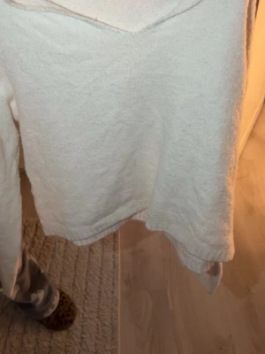 Vit stickad tröja med v-ringning - Mysig vit stickad tröja med v-ringad hals och långa ärmar. Tröjan har en enkel och stilren design med ribbstickade muddar vid ärmslut och nederkant. Perfekt för lager-på-lager och passar till många olika outfits.