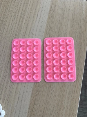 Rosa sugproppsmattor till mobil - Två rosa rektangulära sugproppsmattor i mjukt silikon, perfekta för att fästa mobilen på släta ytor. Nya med klister. Smidiga att ta med och använda i vardagen. 30kr för två stycken