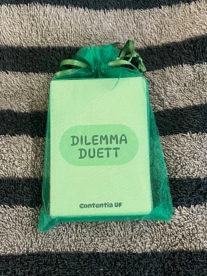 Dilemma Duett kortspel - Kortspelet Dilemma Duett från Contentia UF. Spelet kommer i en grön tygpåse och innehåller flera kort med olika dilemman och spelregler. Perfekt för att utmana vänner och ha roliga diskussioner tillsammans! 😝OBS att färgen i de första bilderna ser annorlunda ut pgr av ljuset 🤗