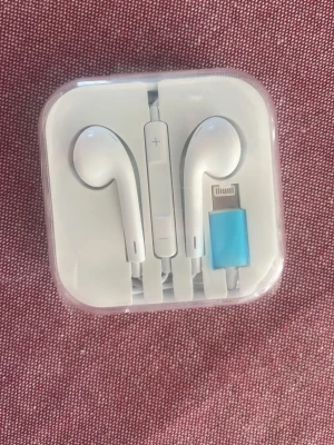 Vita iphone hörlurar med sladd - Säljer ett par vita hörlurar med Lightningkontakt, perfekt för iPhone. Hörlurarna har inbyggd fjärrkontroll och mikrofon på sladden. Kommer i original plastetui. Klassisk Apple-design i plast med rundade öronsnäckor.