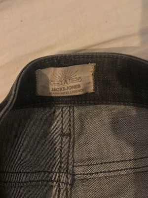 Svarta jeans från Jack & Jones - Säljer ett par svarta jeans från Jack & Jones med diskret tvättad look och raka ben. Klassisk femficksmodell och snygga kontrastsömmar. Perfekta för dig som gillar en enkel men stilren stil.