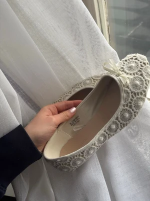 Vita spetsballerinaskor med rosett - Säljer ett par vita ballerinaskor med vacker spetsdetalj och små rosetter framtill. Passar perfekt till skolavslutning eller andra tillställningar☺️☺️säljer pga att de är för stora💞