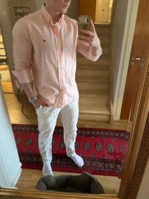 Randig skjorta från Morris Stockholm - Säljer en snygg ljusrosa och vit randig skjorta från Morris Stockholm i storlek L. Skjortan har klassisk krage, långa ärmar och knappar framtill. Tillverkad i mjuk bomull, perfekt för en clean och stilren look.