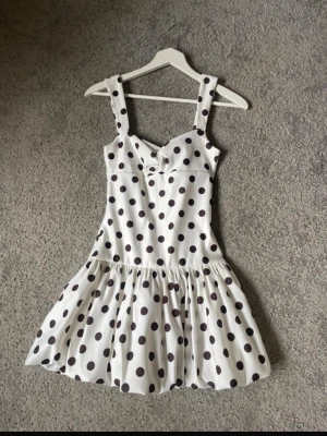  Ny  slutsåld Vit klänning med svarta prickar från Zara  - Supersöt vit klänning med stora svarta prickar och breda axelband. Klänningen har en markerad midja och en volangig kjol som ger en lekfull look. Materialet ser ut att vara mjukt och lätt, perfekt för varma dagar. Dragkedja i ryggen för enkel påklädning.