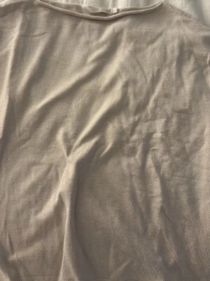 Beige stickad tröja från 157 - En enkel och stilren beige stickad tröja från 157. Tröjan har rund halsringning som är off shoulder och är gjord i ett mjukt, tunt stickat material som passar perfekt till lager på lager. Perfekt basplagg för din garderob.