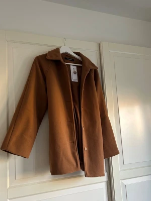 Klassisk brun kappa - Stilren brun kappa från Gina Tricot  i rak modell med krage och knäppning framtill. Band att knyta om jackan🤎