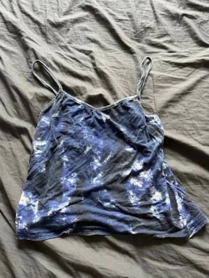 Blå batikmönstrad linnetopp - Säljer en blå och svart batikmönstrad linnetopp med tunna axelband. Toppen har en avslappnad passform och är perfekt för varma dagar. Materialet känns mjukt och lätt mot huden.