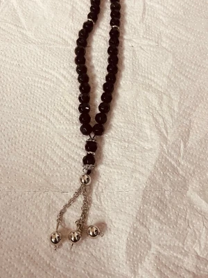 Svart pärlhalsband med silverdetaljer - Snyggt halsband med svarta, facetterade pärlor och silverfärgade detaljer. Halsbandet har en unik design med hängande kedjor och silverkulor längst ner. Perfekt accessoar för att lyfta din outfit med en cool och elegant touch.