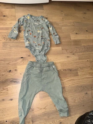 Grönt bodyset med djurmönster - Grönt bodyset med djurmönster Säljer ett set med långärmad body och byxor i mjuk grön bomull. Bodyn har gulligt djurmönster i flera färger och tryckknappar i grenen för enkel påklädning. Byxorna är enfärgade gröna med resår i midjan och muddar vid bensluten.
