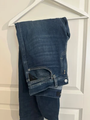 Replay jenas - Snygga mörkblå jeans från Replay med klassisk femficksdesign och diskreta slitningar. Jeansen har raka ben och detaljer i silverfärgad metall. Perfekta för en stilren och avslappnad look.