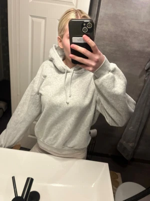 Ljusgrå hoodie med huva - En stilren ljusgrå hoodie med huva och dragsko. Hoodien har en relaxed fit, ribbade muddar vid ärmslut och midja samt mjukt material som känns skönt mot huden. Perfekt för en chill och avslappnad look.