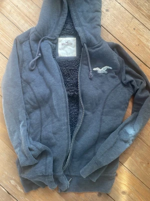 Mörkgrå hoodie från Hollister - Mörkgrå hoodie från Hollister med dragkedja och fluffigt foder på insidan säljes. Klassisk logga på bröstet. Skick 8/10. Vid frågor skicka dm