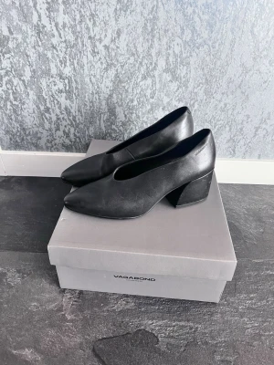 Svarta pumps från Vagabond - Stilrena svarta pumps från Vagabond med rundad tå och bred klack. Skorna är tillverkade i slätt läder och har en klassisk, minimalistisk design som passar till många olika looks. Perfekta för dig som gillar tidlös stil och komfort.