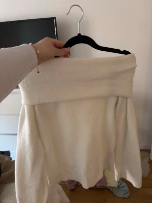 Off shoulder vit stickad tröja - Säljer en vit stickad off shoulder-tröja med bred krage. Tröjan har långa ärmar och ribbade muddar vid ärmslut och nederkant. Perfekt för dig som vill ha en enkel men snygg stickad topp till hösten eller vintern.