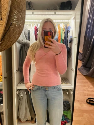 Rosa omlottstickad tröja från E-vie - Säljer en rosa stickad omlottopp från E-vie med långa ärmar och knytband i midjan. Tröjan har en djup V-ringning och mjukt material som sitter snyggt på kroppen. Perfekt att styla med jeans eller kjol för en trendig look. Storlek 10-12 år men skulle säga att den passar för S!