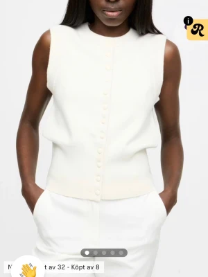 Vit stickad väst med knappar från Bikbok - Stilren vit stickad väst med rund hals och dekorativa knappar framtill. Västen har en rak passform och är perfekt att styla över en skjorta eller t-shirt för en clean look.