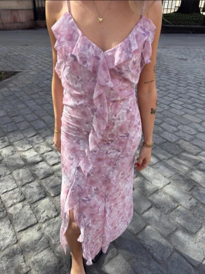  blommig långklänning - mer som strl 36/38 - Liten i strl. Mer som strl 36/38. Romantisk långklänning i ljusrosa toner med blommigt mönster och volangdetaljer framtill. Klänningen har tunna axelband, öppen rygg med knyt och en luftig passform. Perfekt för sommarens alla tillfällen.