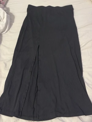 Svart långkjol med slits - Säljer en svart långkjol med diskret ribbad struktur och slits framtill. Kjolen har en enkel och stilren design som passar till många olika looks. Materialet känns mjukt och följsamt mot kroppen.