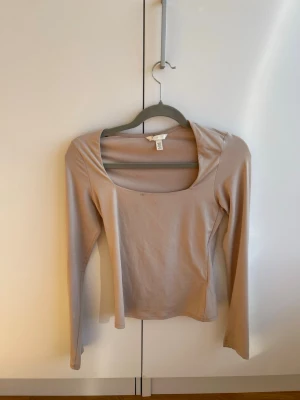Beige långärmad topp från H&M - Säljer en stilren beige långärmad topp från H&M med fyrkantig urringning. Toppen har en slim passform och är tillverkad i mjuk bomullsmix som känns skön mot huden. Lite smutsig och går ej bort i tvätt. 