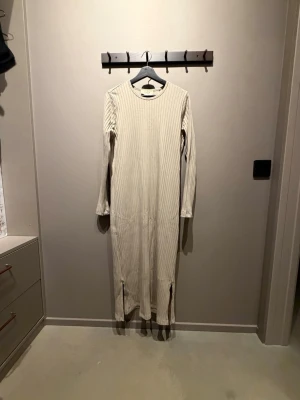 Lång ribbad beige klänning - En beige långklänning från A PART OF THE ART i storlek xs med en liten slits på båda sidor längst ner.