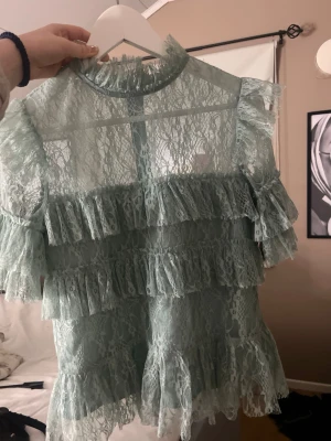 By malina blus  - Snygg ljusgrön blus i spets med volangdetaljer och hög krage. Nypris ca 2000, (de e lite dåligt ljus) 