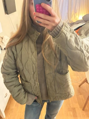 Quiltad grön jacka från Zara - Säljer en quiltad grön jacka från Zara i storlek XS. Jackan har en loose passform, hög krage och stora fickor framtill. Perfekt för lager på lager och har en snygg vågig quiltad design som sticker ut.
