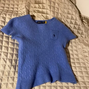 Blå kortärmad tröja från Ralph Lauren - Säljer en snygg blå kortärmad tröja från Ralph Lauren. Tröjan har en liten bröstficka med den ikoniska loggan och ribbade kanter. Perfekt för en stilren look! Krympt i tvätt