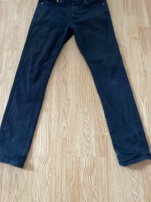 Jack & Jones jeans  - Säljer ett par svarta jeans med rak passform och klassisk femficksdesign. Jeansen har knappgylf och är tillverkade i ett mjukt denimtyg som ger en skön känsla. Perfekta för dig som gillar en enkel och stilren look.