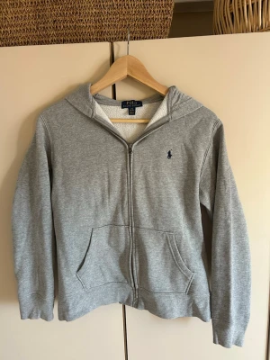 Grå zip hoodie från Polo Ralph Lauren - Klassisk grå hoodie med dragkedja från Polo Ralph Lauren. Hoodien har huva, två fickor framtill och den mörkblå loggan broderad på bröstet. Tillverkad i mjuk bomullsblandning som känns skön mot huden. Passar princip till allt och ger en  avslappnad look. (pris går att diskutera). 💗