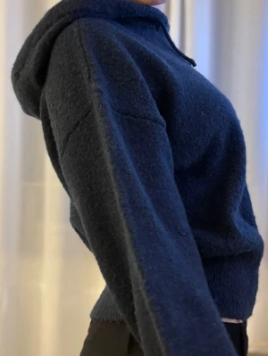 Mörkblå hoodie i mjukt material - Mysig mörkblå hoodie med huva och dragsko. Tillverkad i ett fluffigt, stickat material som känns riktigt skönt mot huden. Modellen har ribbade muddar vid ärmslut och midja för en snygg passform. Perfekt för dig som gillar en avslappnad och trendig stil.