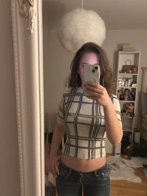 Rutig croppad topp med korta ärmar - Säljer en croppad topp med korta ärmar och rutigt mönster i vitt och grått. Toppen har en slim passform och är perfekt för dig som gillar trendiga och bekväma plagg. Materialet känns mjukt och stretchigt, troligen bomull eller polyester.