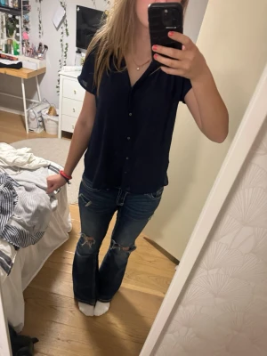 Svart blus med knappar - Säljer en stilren svart blus med knappar framtill. Den har en avslappnad passform och korta ärmar, perfekt för både vardag och fest. Blusen är i mycket bra skick och passar till de flesta outfits.