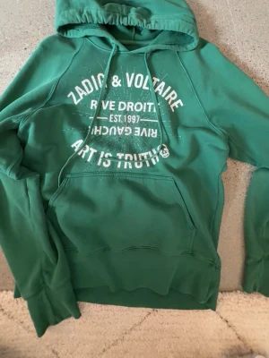 Grön hoodie Zadig & Voltaire - Snygg grön hoodie från Zadig & Voltaire med vit text och glittriga detaljer framtill. små defekter, lappen lossar, glittret har tappats. (kolla bilder) men den är fortfarande super fin och har inga fläckar! pris kan diskuteras❤️
