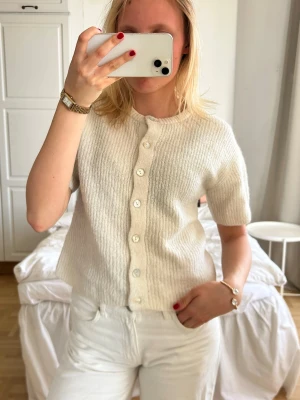 Vit kortärmad kofta med knappar💖💖 - Säljer en söt vit kofta med korta ärmar och rund hals. Koftan har ribbad struktur och knäpps med vita knappar framtill. Perfekt att styla med jeans eller kjol för en clean look.